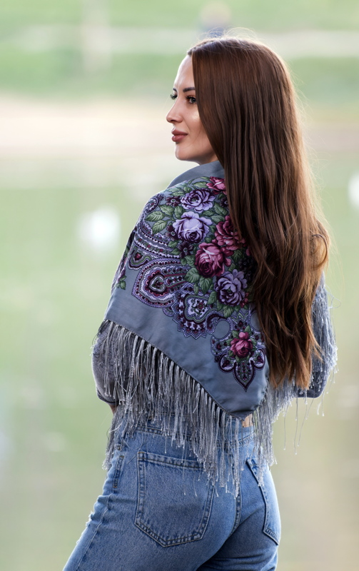 9 - A person wearing a grey floral-print traditional Slavic-style shawl with long fringe and blue jeans